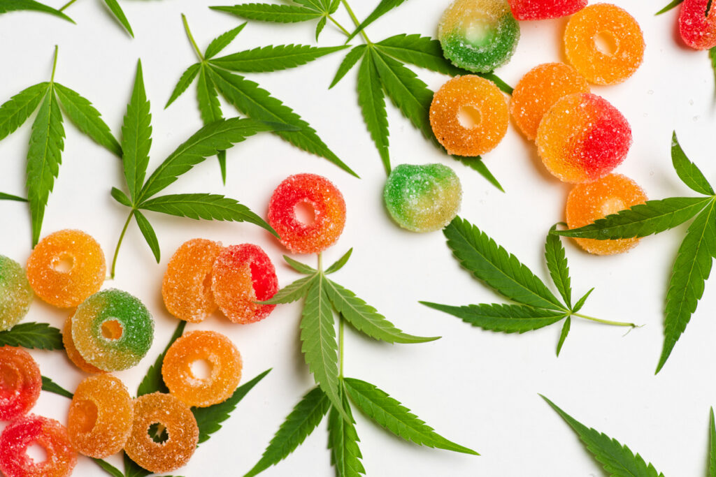 Colorful gummies with cannabis leaves on white background.