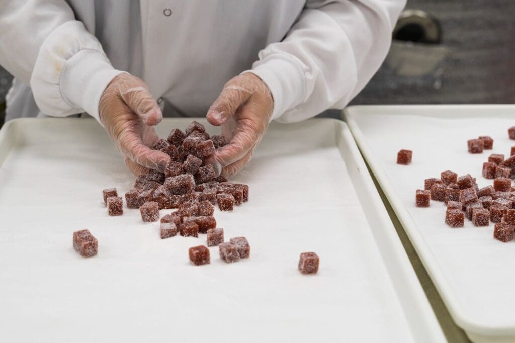 Person arranging sugar-coated candy cubes on tray.