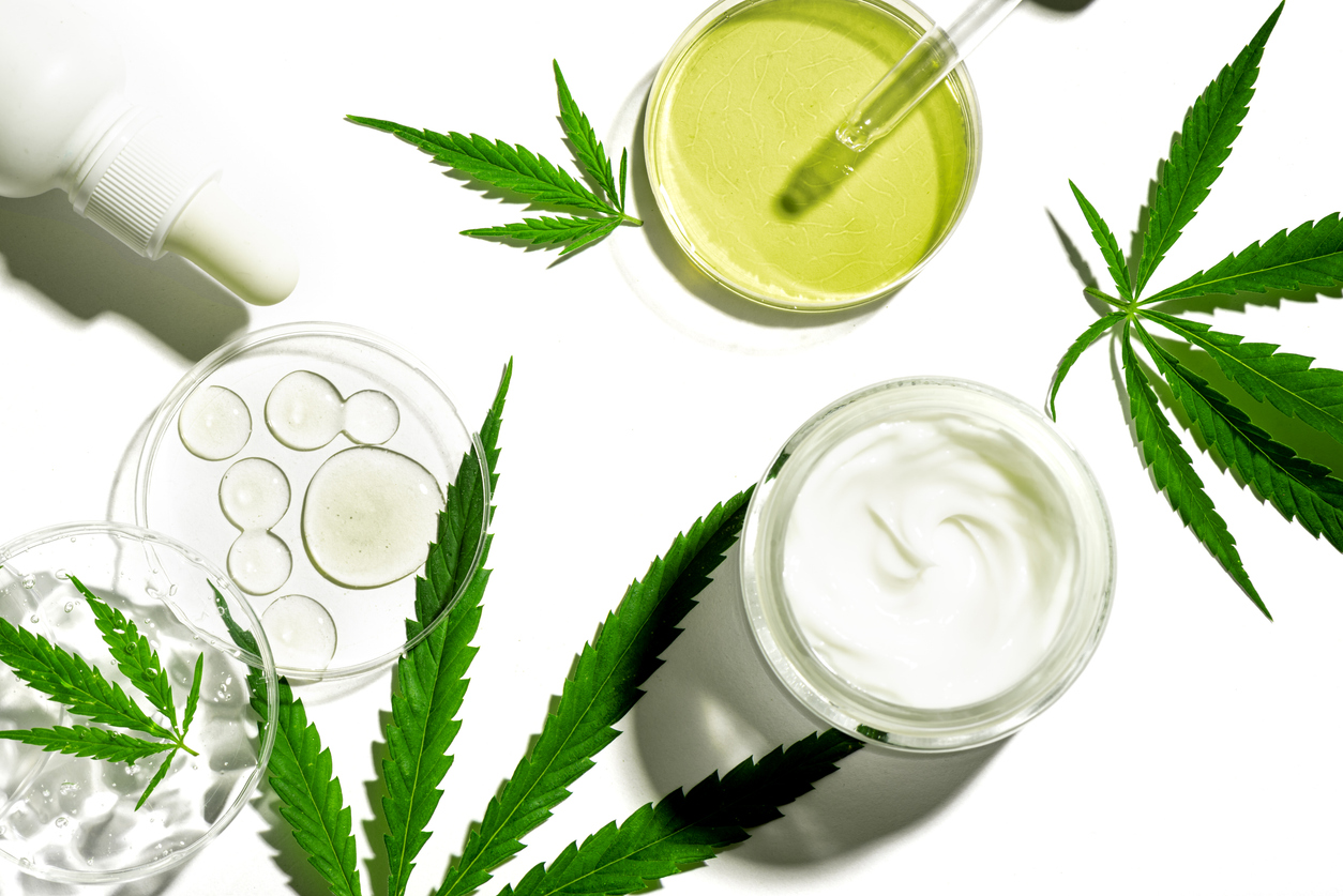 Cannabis leaves with skincare products on white background.