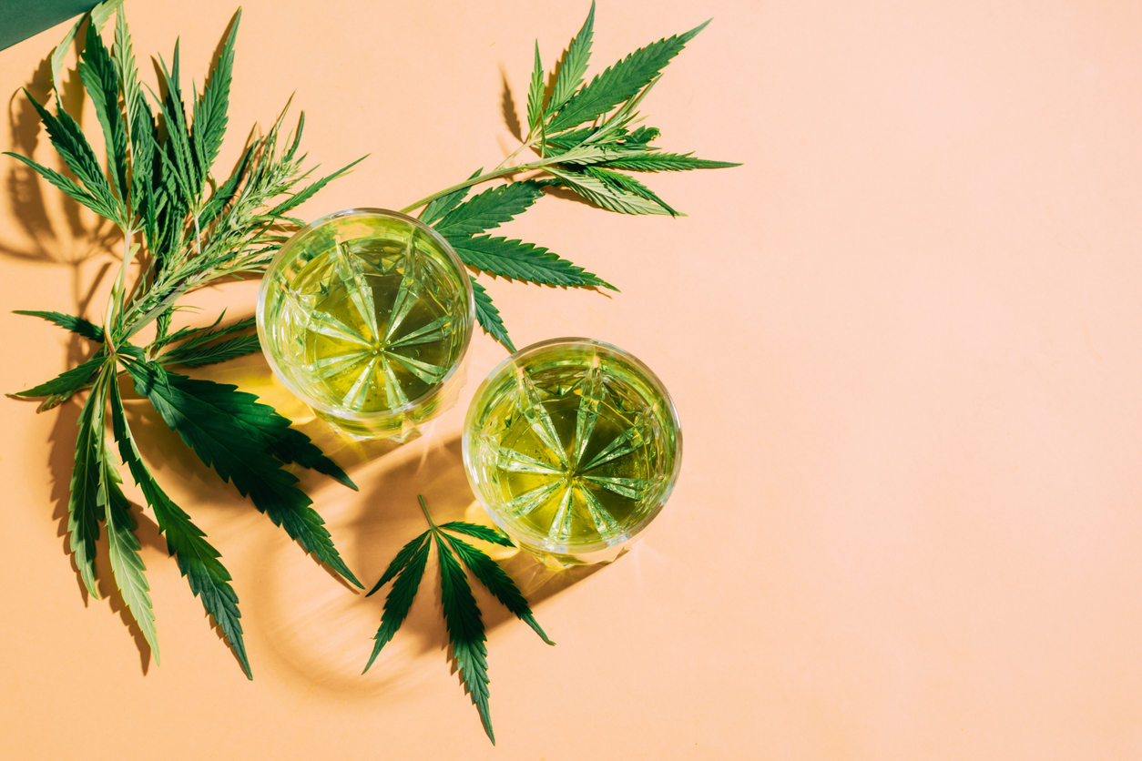 Herbal drinks with cannabis leaves on peach background.