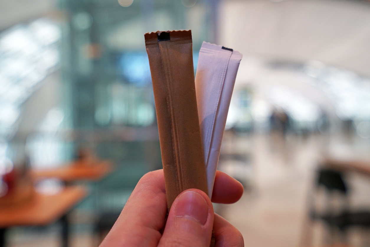 Hand holding brown and white sugar packets.