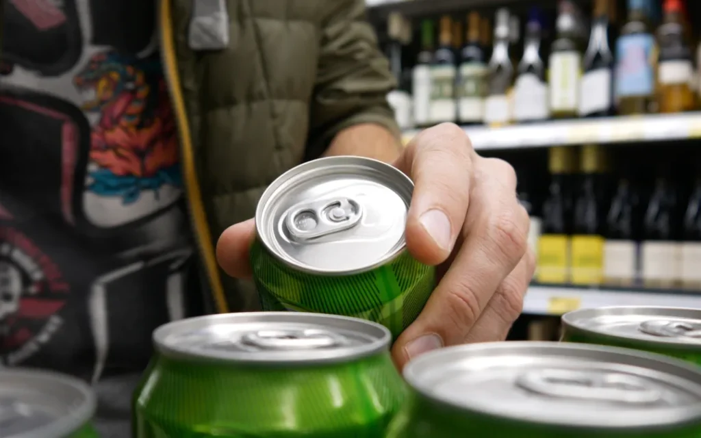 Close-up of a male buyer's hand taking a green can of beer in alcohol department